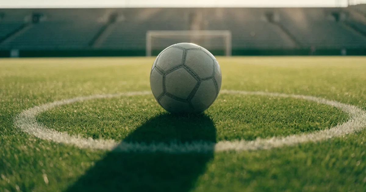 Uma bola de futebol no ponto central de um relvado, à luz da manhã