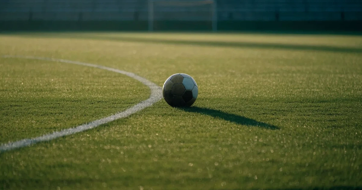 Uma bola de futebol no ponto central de um relvado, à luz da manhã