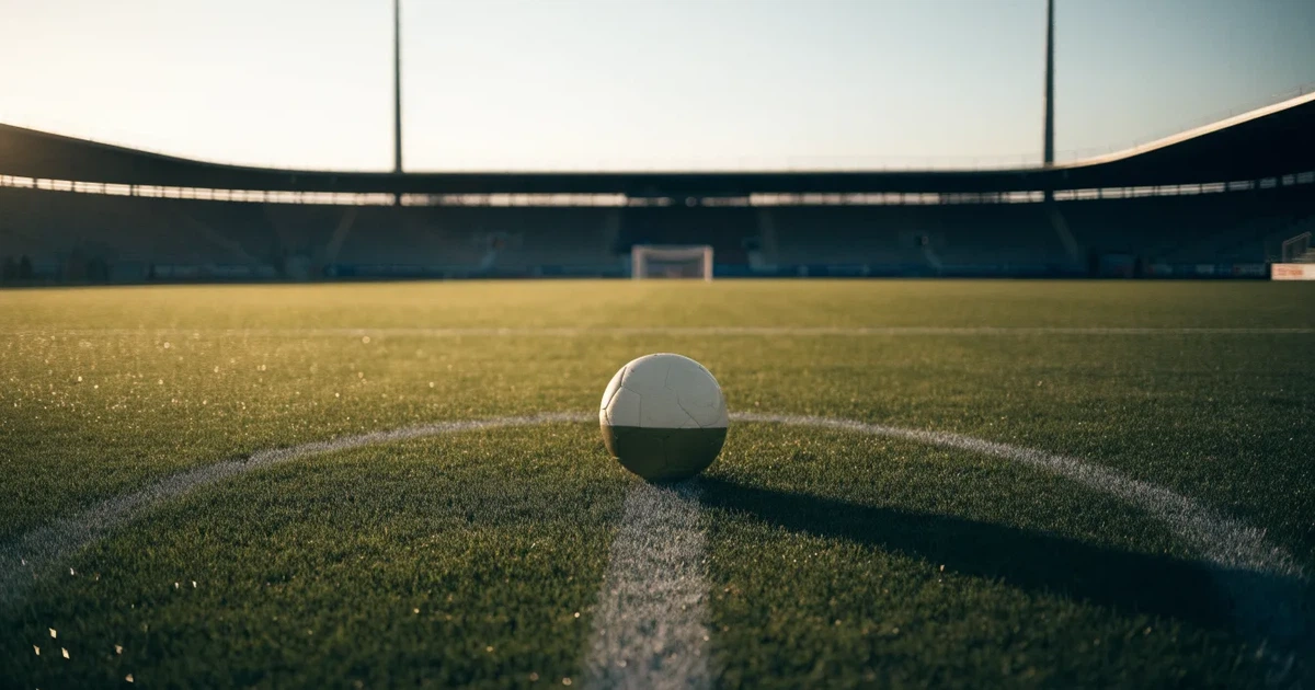 Uma bola de futebol no ponto central de um relvado, à luz da manhã